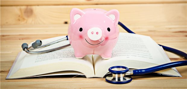 Sparschwein und Stethoskop liegen auf einem Buch.