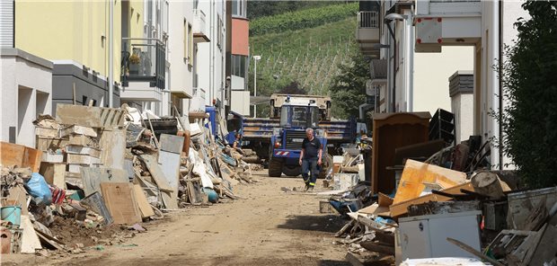 Bad Neuenahr: Straße, in der sich der Schutt etwa mannshoch türmt; Es wird allerdings schon aufgeräumt - ein Fahrzeug mit Frontlader fährt Schutt in einen Hänger.