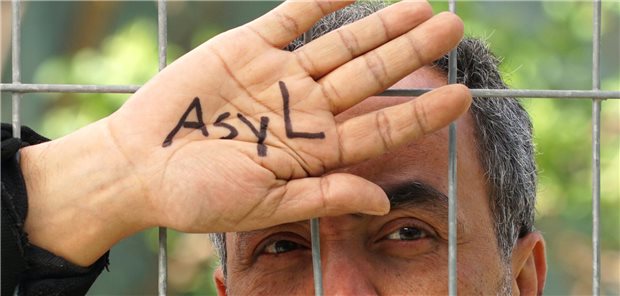 Mensch hinter einem Zaun mit der Aufschrift "Asyl" auf seiner Hand.