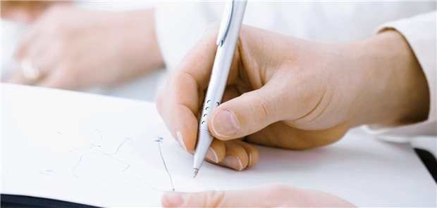 Weiterbildung in der Bürokratie-Falle Eine Hand schreibt mit einem Kugelschreiber auf Papier.