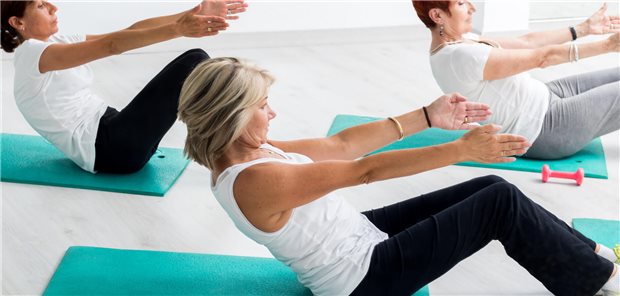 Drei Frauen mittleren Alters bei einer Bauchmuskelübung im Fitnessstudio.