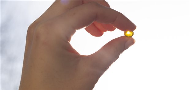 Nahaufnahme einer Vitamin-D-Kapsel in der Hand eines Menschen die gegen das Sonnenlicht gehalten wird.