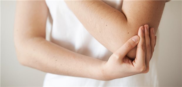 Eine junge Frau fasst sich an ihren schmerzenden Ellenbogen.