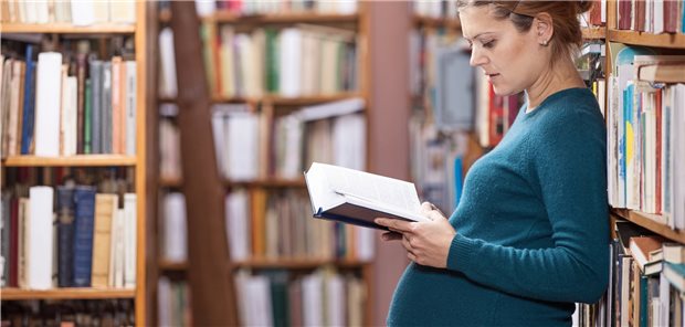 Schwangere Frau liest in der Bibliothek.