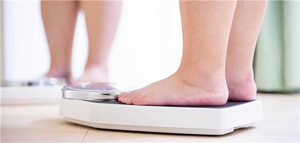 Eine übergewichtige Frau steht vor einem Spiegel und misst ihr Gewicht auf einer Waage.