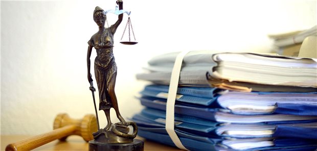 Die modellhafte Nachbildung der Justitia steht in einem Raum eines Richters neben einem Holzhammer und einem Aktenstapel.