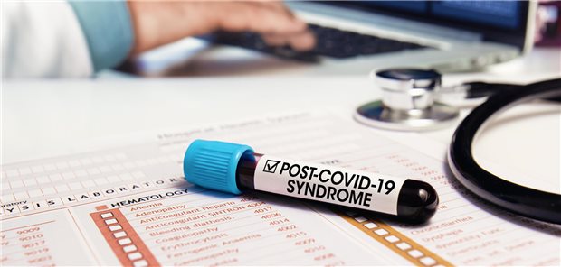 Kleine Flasche mit Aufschrift "Post-COVID-19-Syndrom" auf dem Tisch eines Arztes