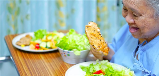 Eine ältere Frau hält ein ganzes Steak hoch, das sie auf eine Gabel aufgespießt hat.