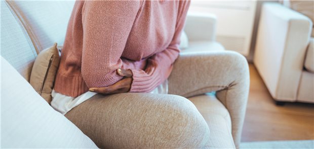 Eine frau sitzt auf einer Couch und hält sich den Bauch vor Schmerzen