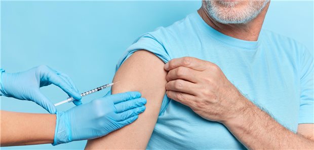 Ein Mann mit weißem Bart bekommt eine Impfung in den Arm.