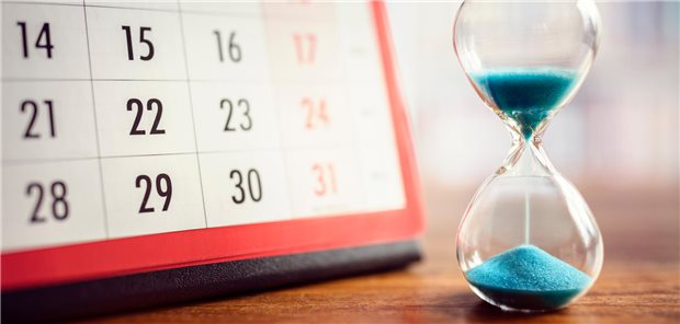 Eine Sanduhr steht neben einem Aufstellkalender. Der Sand rinnt.