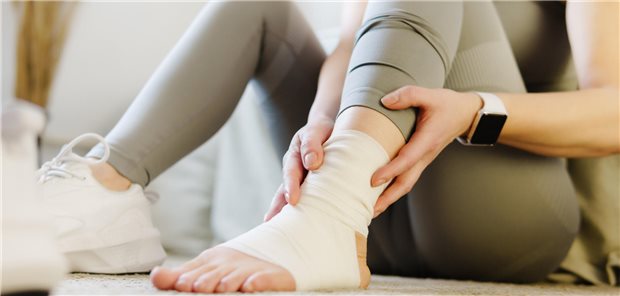 Fersenkick hilft, Schmerzen am verstauchten Sprunggelenk zu lindern Eine Frau hält mit beiden Händen ihren schmerzenden verstauchten Knöchel.