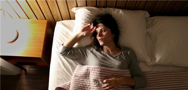 Eine Frau mit Insomnie liegt in ihrem Bett und kann nicht einschlafen.