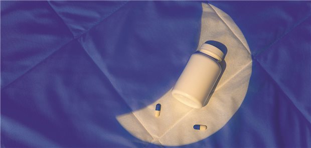 Eine Tablettendose liegt auf dem Bett. Ein Lichtkegel in der Form des Mondes scheint darauf.