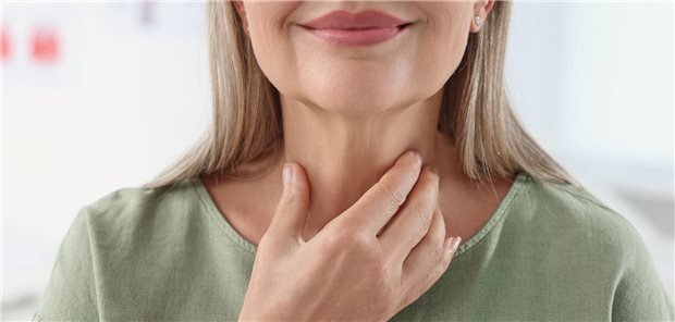 Eine Frau fasst sich mit der Hand an den Hals.