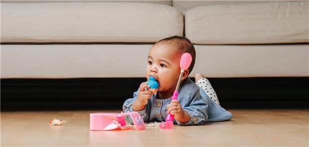 Ein kleines Kind spielt mit kleinteiligem Speilzeug und führt sich dieses an den Mund.