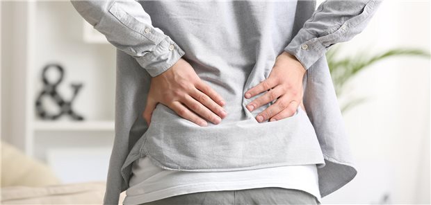 Ein Mensch ist von hinten zu sehen, der sich an den Rücken greift.