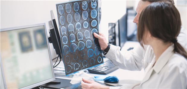 Zwei Ärzte, ein Mann und eine Frau, untersuchen ein MRT-Bilder des Gehirns eines Patienten.