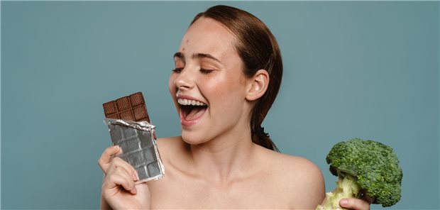 Frau mit Pickeln posiert mit Schokolade und Brokkoli isoliert vor blauem Hintergrund
