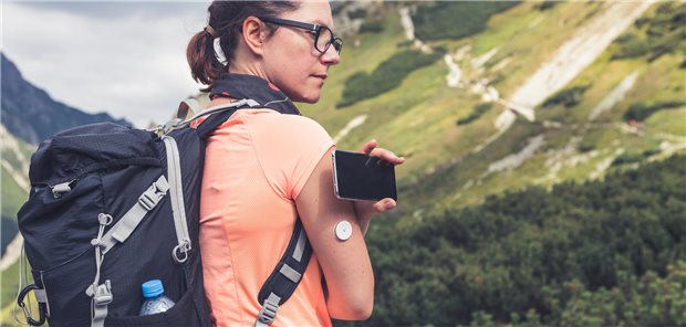 Frau ruft ihren Blutzuckerwert per Smartphone ab, während sie in den Bergen ist.