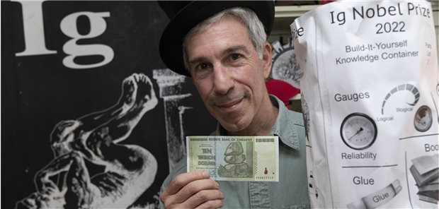 Moderator Marc Abrahams mit dem Preisgeld: einem echten Trillionen-Dollar-Geldschein – aus Zimbabwe. Daneben der Ig-Nobelpreis, den die Gewinner zugeschickt bekommen und selbst zusammenbauen müssen.