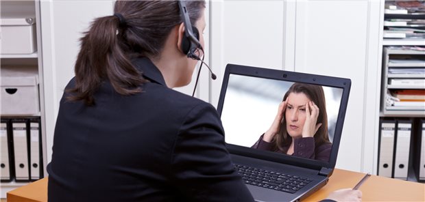 Videosprechstunden: Therapeuten und AOK warnen vor Folgen des geplanten Digital-Gesetzes Frau mit Headset vor einem Laptop, der zeigt, wie sich eine andere Dame an die Schläfen fasst.