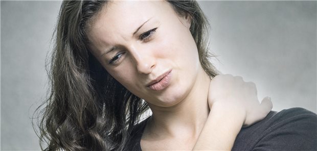 Eine Frau fasst sich mit dem Arm an die linke Schulter.