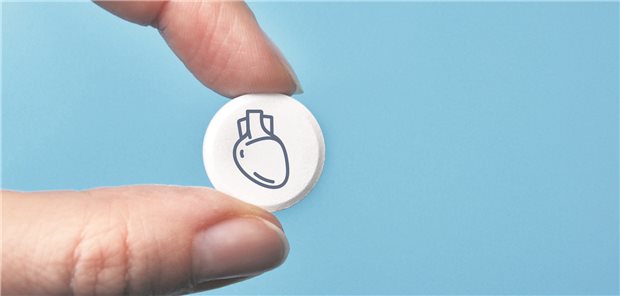 Eine Person hält eine weiße Tablette zwischen den Fingern. Auf der Tablette ist ein Herz abgedruckt. 