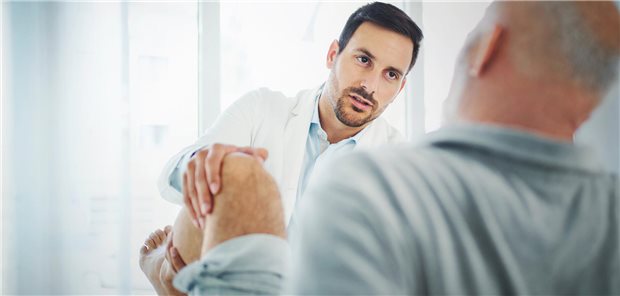 Ein Arzt untersucht das Knie eines Patienten.