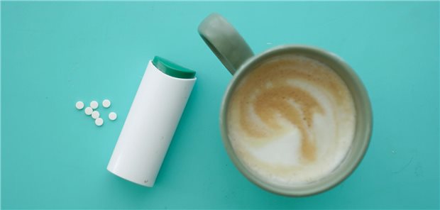 Eine Packung Süßstoff liegt neben einer Kaffeetasse.