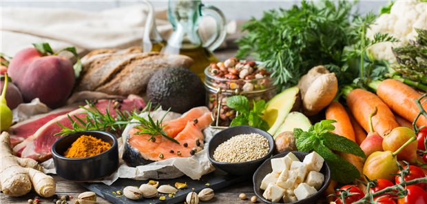 Auf einem tisch liegt eine Vielzahl an Lebensmitteln, wie Käse, Lachs, Karotten, Pistazien, Tomaten, Brot, Avocado