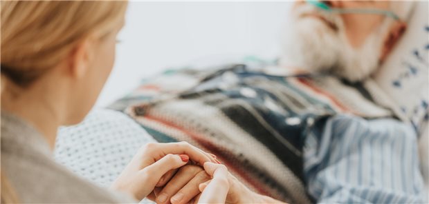 Frau hält einer Person im Bett die Hand.