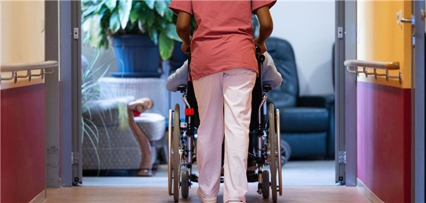 Auf einem Klinikflur schiebt eine Pflegekraft eine ältere Patientin.