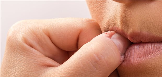 Nahaufnahme einer Frau, die an ihrem Daumennagel kaut.