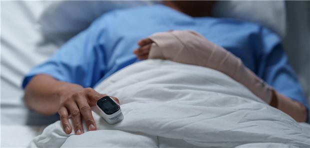Eine Person liegt in einem Krankenhausbett und trägt ein Pulsoximeter am rechten Zeigefinger.