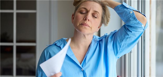 Nach der Menopause: Elinzanetant bessert in Studie Hitzewallungen und Schlafprobleme Eine ältere Frau fächelt sich mit einem Blatt Papier Luft zu, während sie sich mit der anderen Hand die Haare hochhält.