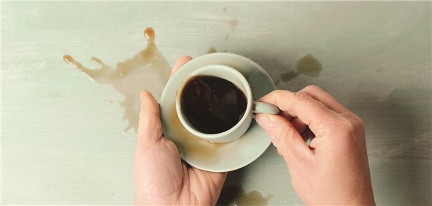Zwei Hände halten eine Kaffeetasse. Kaffee wurde über den Tisch verschüttet.