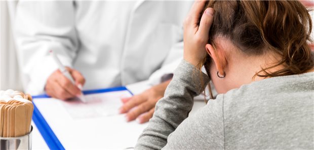 Eine junge Frau sitzt beim Arzt und hält sich verzweifelt den Kopf.  