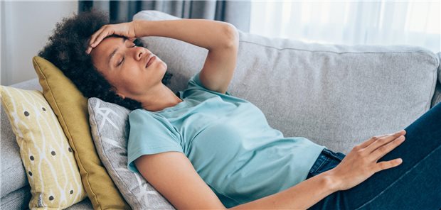 Eine Frau liegt auf der Couch und hält sich den Kopf als würde er schmerzen. 